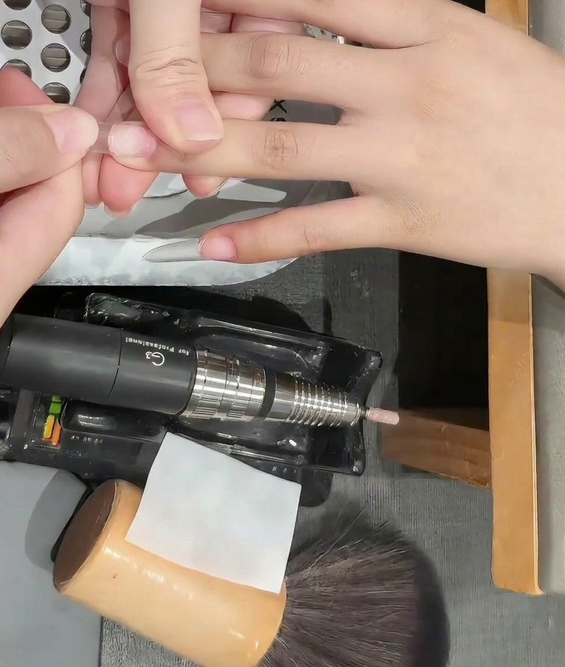 Ein Nagelbuffer wird auf der Oberfläche eines klaren Nagel-Tips verwendet, um den Glanz zu entfernen.
