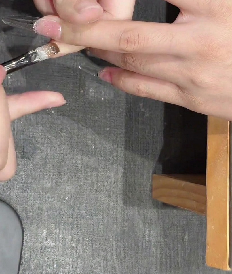 Eine Pinzette platziert kleine, metallische sternförmige Glitzerpartikel auf einen mit Gel beschichteten Nagel.