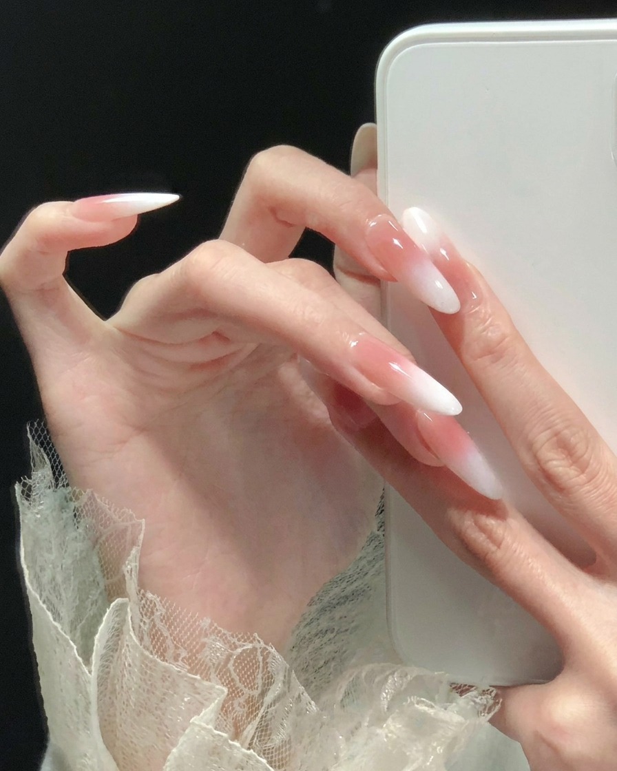 Seitenansicht von langen, mandelförmigen Nägeln mit einem rosa-weißen Ombré-Finish.