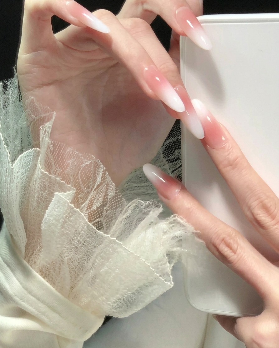 Eine Hand mit gespreizten Fingern zeigt einen einheitlichen rosa-weißen Ombré-Verlauf auf allen langen, mandelförmigen Nägeln.