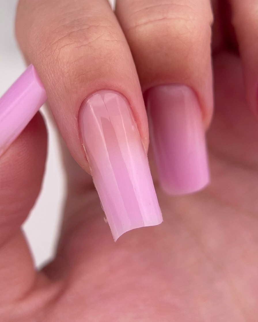 Nahaufnahme eines Fingers, auf dem ein klarer, glänzender Base Coat auf den Nagel aufgetragen wurde.