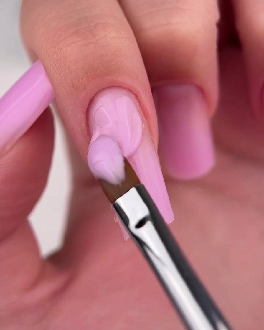 Nahaufnahme eines Pinsels, der den Ombré-Übergang auf einem rosa Ombré-Nagel glättet.