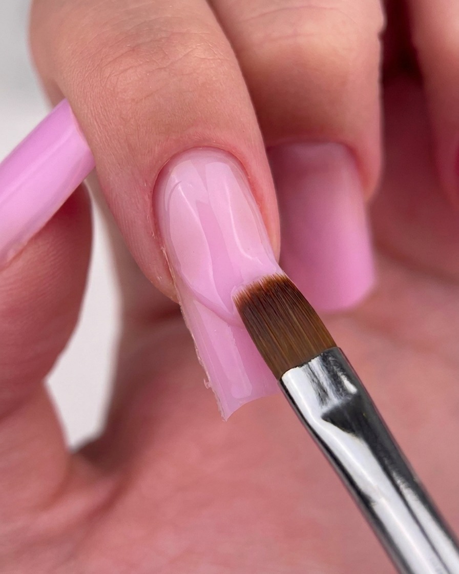 Ein feiner Liner-Pinsel reinigt vorsichtig den Rand des rosa Gels an der Nagelhaut.