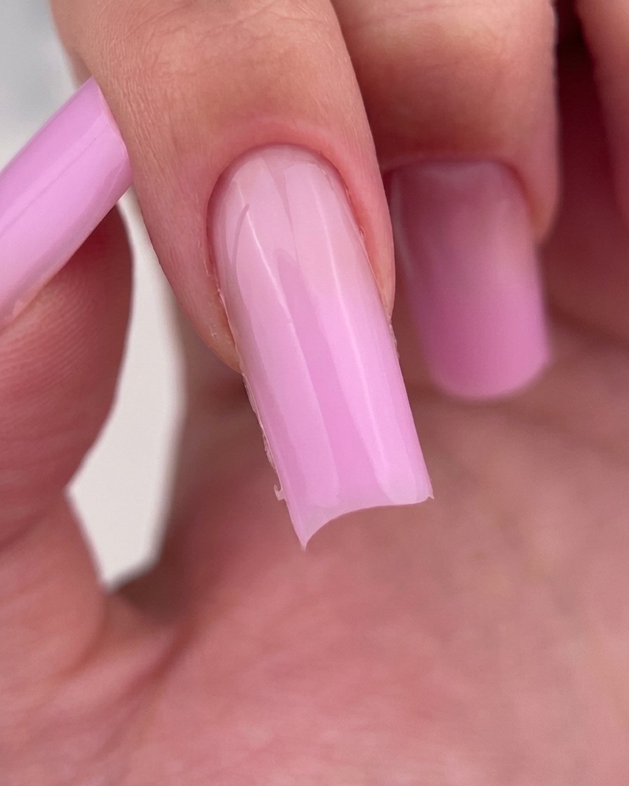 Nahaufnahme einer Nagelfeile, die die freie Kante eines quadratisch geformten, hellrosa Gelnagels verfeinert.
