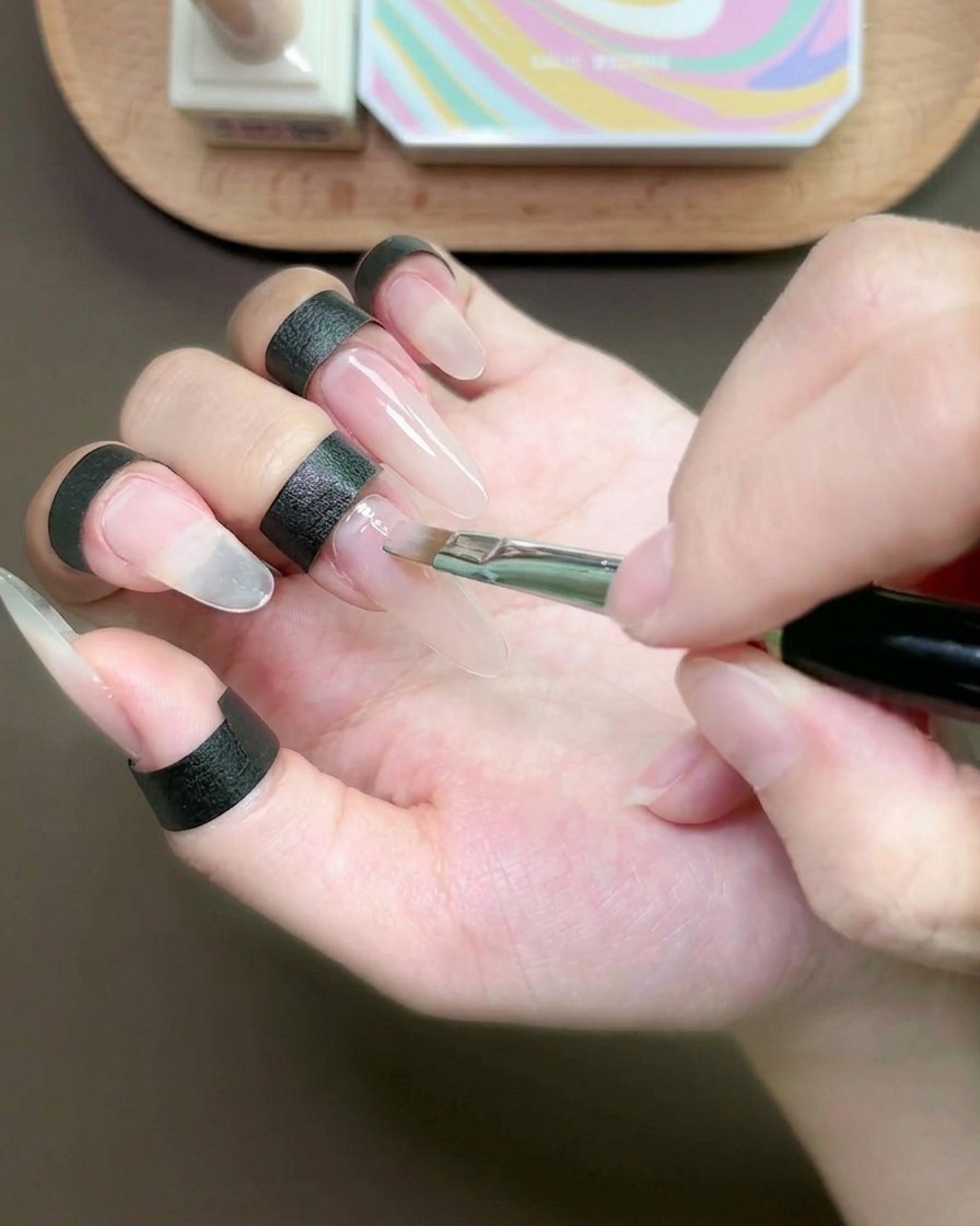 Ein flacher Pinsel trägt eine dünne Schicht Nude-Gel auf den Mittelfingernagel auf.
