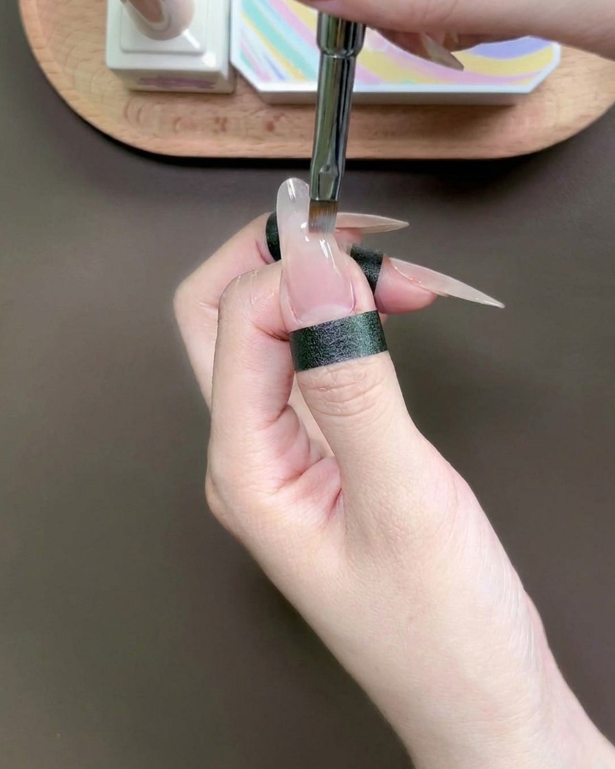 Ein spezielles Tupfwerkzeug platziert einen Tropfen blaues Gel auf die Spitze eines Fingernagels.