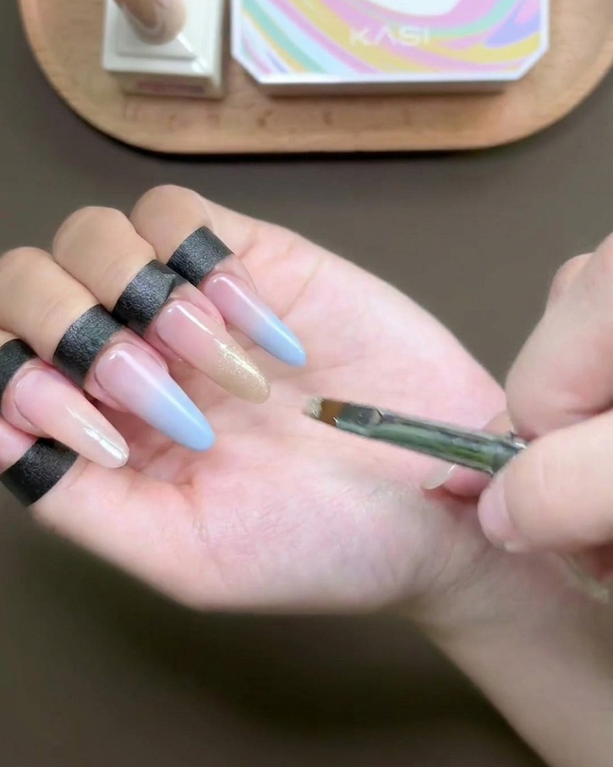 Ein flacher Pinsel trägt schimmerndes Champagner-Cat-Eye-Gel auf eine Fingernagelspitze auf.