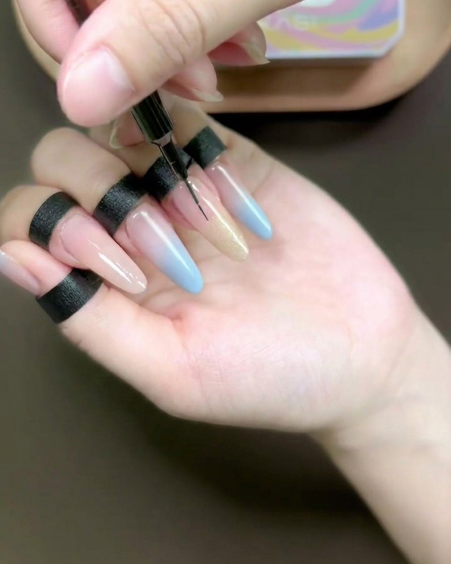 Nahaufnahme eines feinen Liner-Pinsels, der champagnerfarbenes Cat-Eye-Gel auf einen langen, mit Schablone verlängerten Ringfinger verblendet.