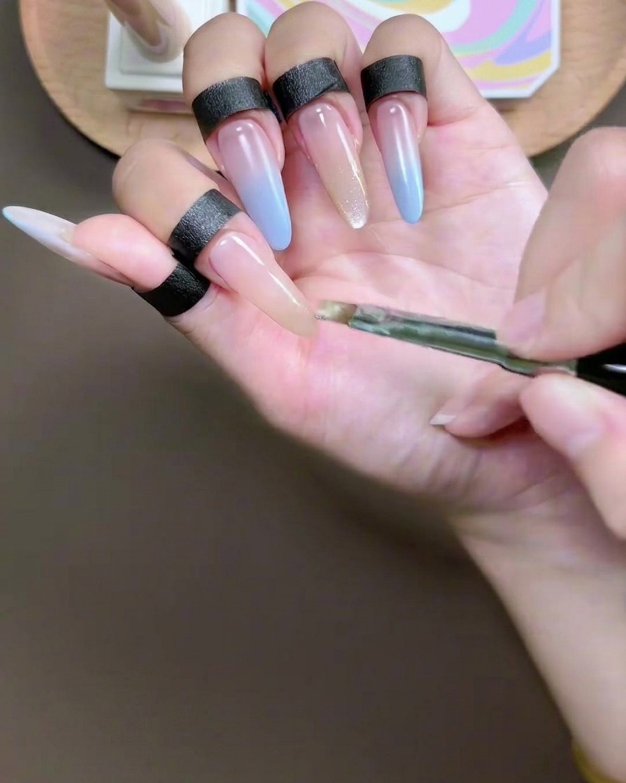 Ein Gelpinsel trägt ein pigmentiertes Champagner-Cat-Eye-Gel auf die Spitze eines Zeigefingernagels auf.
