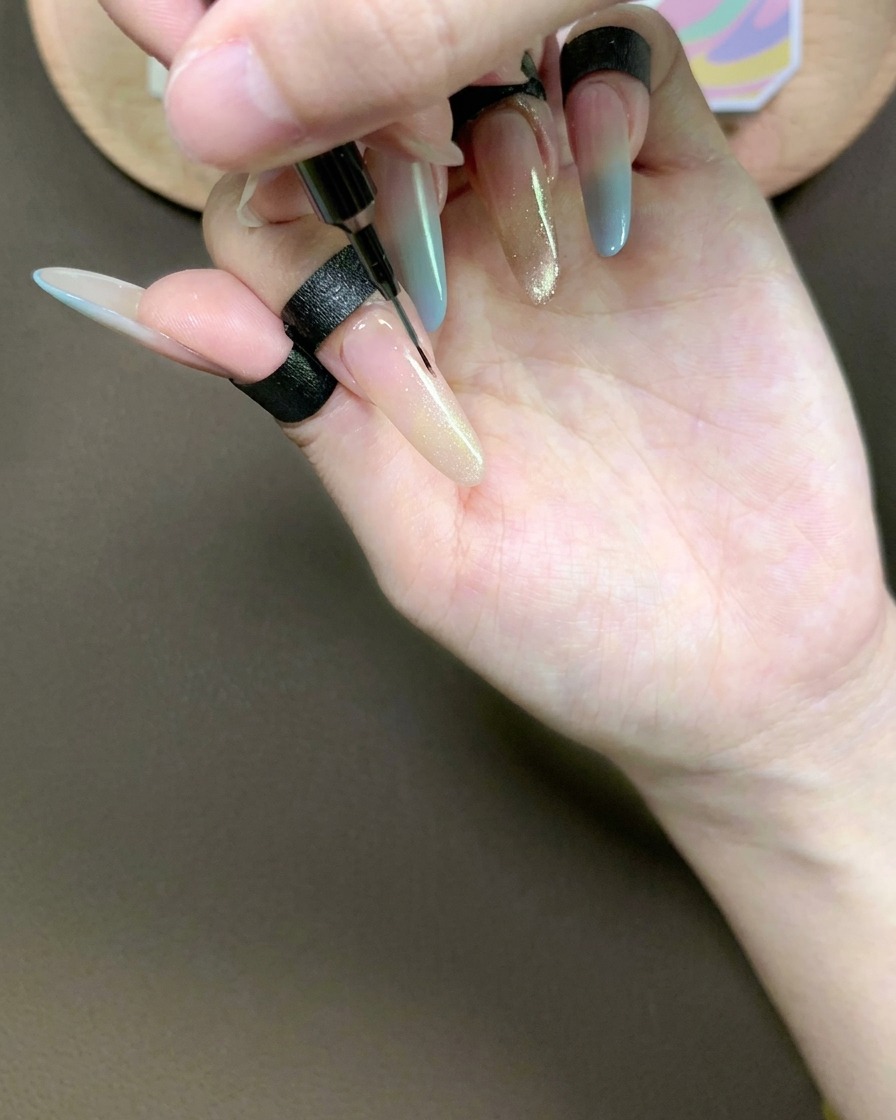 Ein feiner Liner-Pinsel zieht sanft durch das Cat-Eye-Gel auf dem Zeigefinger, um einen weichen, spitz zulaufenden Farbverlauf zu erzeugen.