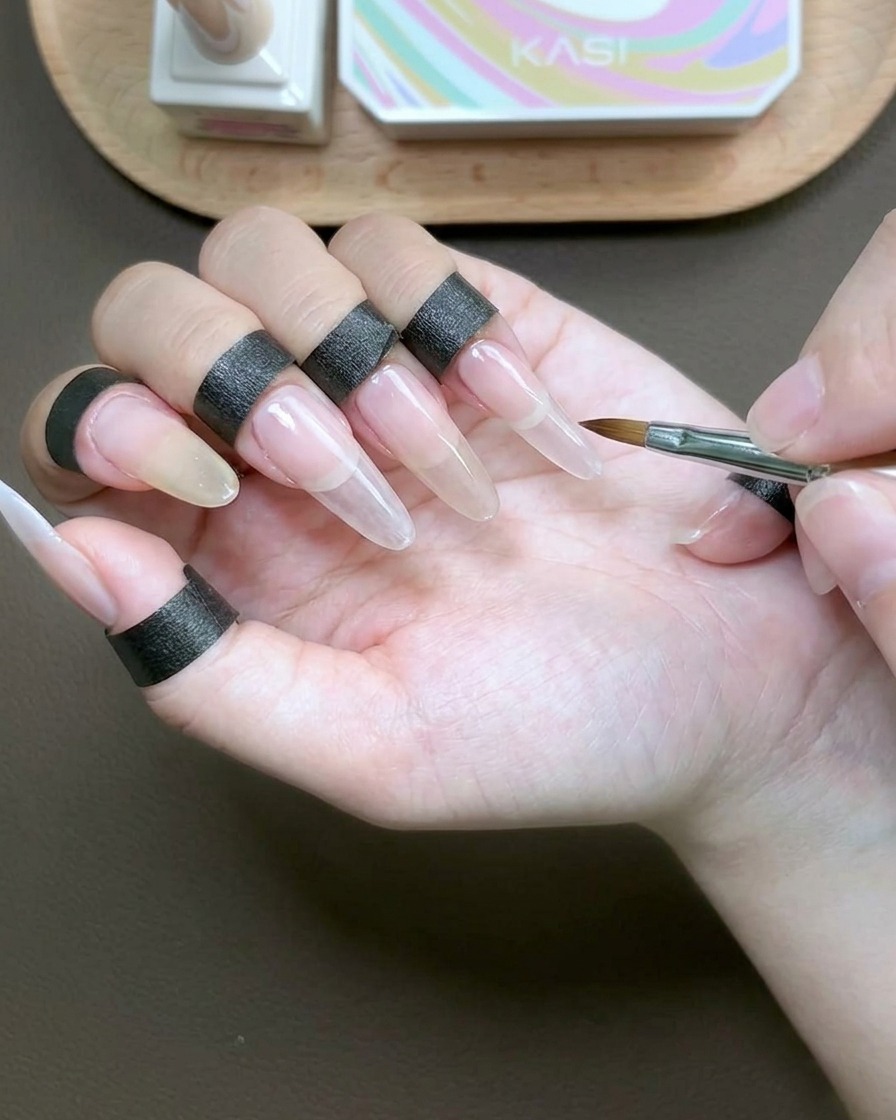 Ein Pinsel trägt ein klares, viskoses Aufbaugel zur Versiegelung über die gesamte Oberfläche des Zeigefingernagels auf.