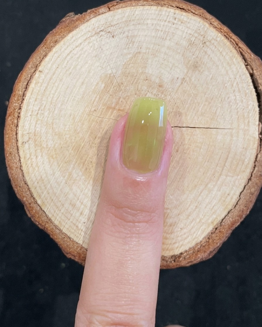 Nahaufnahme eines Pinsels beim Auftragen von transparentem grünem Gel auf einen Naturnagel.
