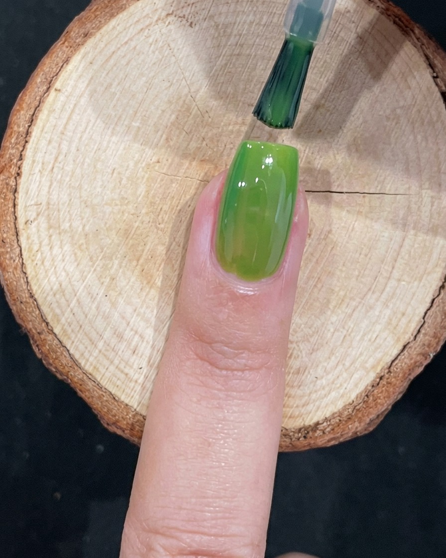 Ein Pinsel führt präzise grünes Gel in der Nähe des Nagelbetts auf.