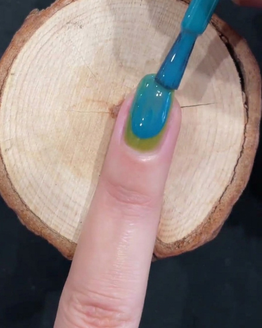 Ein Pinsel erzeugt einen sanften Farbverlauf auf einem grün-blauen Nagel.