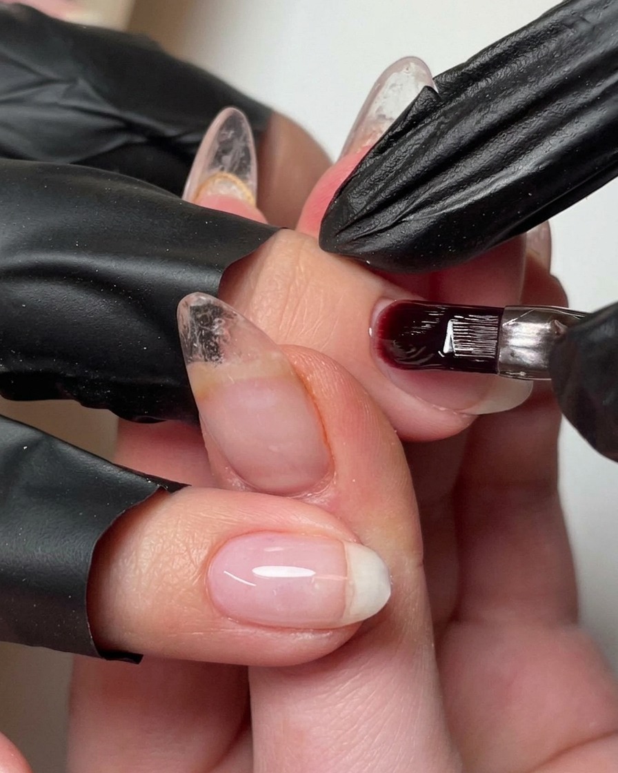 Ein Pinsel gibt einen kleinen Tropfen Aufbaugel auf den Nagel, um den Apex zu verfeinern.