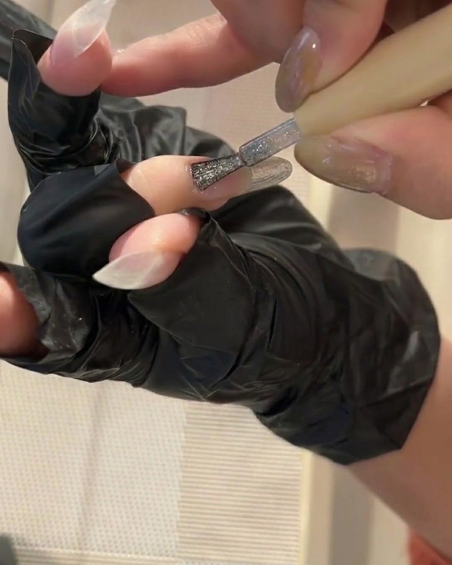 Ein kleiner Pinsel trägt eine dünne Schicht klaren Gel-Base-Coats auf einen sauberen Nagel auf.