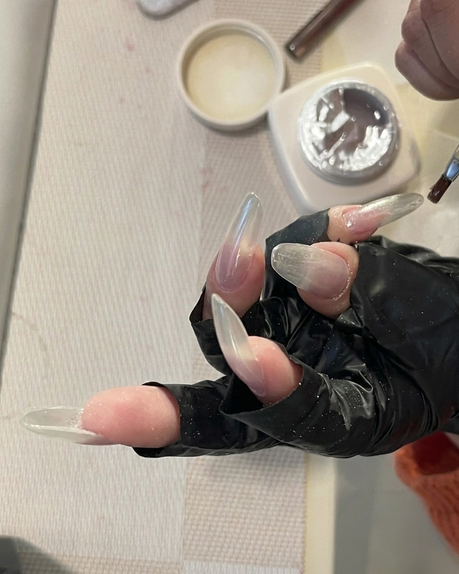 Eine Hand mit langen, klaren Nägeln ruht in einer professionellen UV/LED-Nagellampe, während die Nägel vom Licht beleuchtet werden.