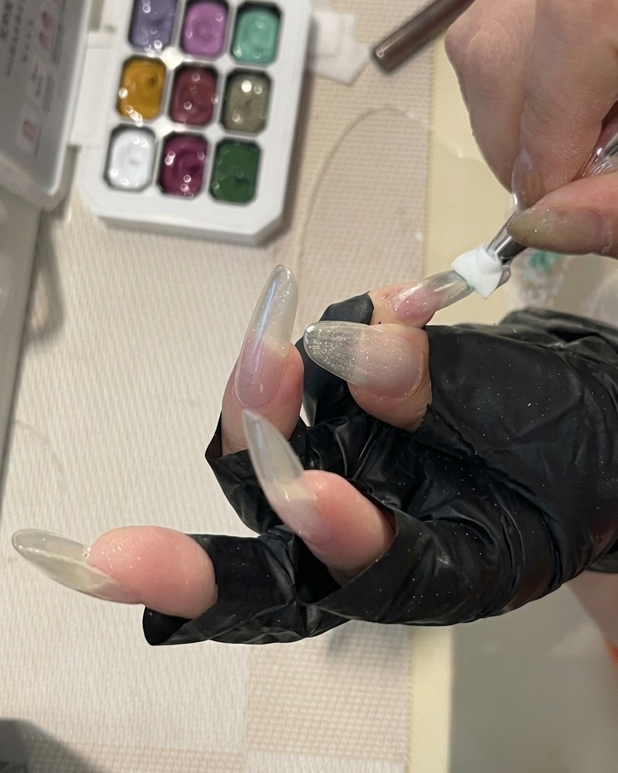 Ein Nagelpinsel verblendet mintgrünes Gel auf der Oberfläche eines langen, strukturierten Nagels zu einem zarten Verlauf.