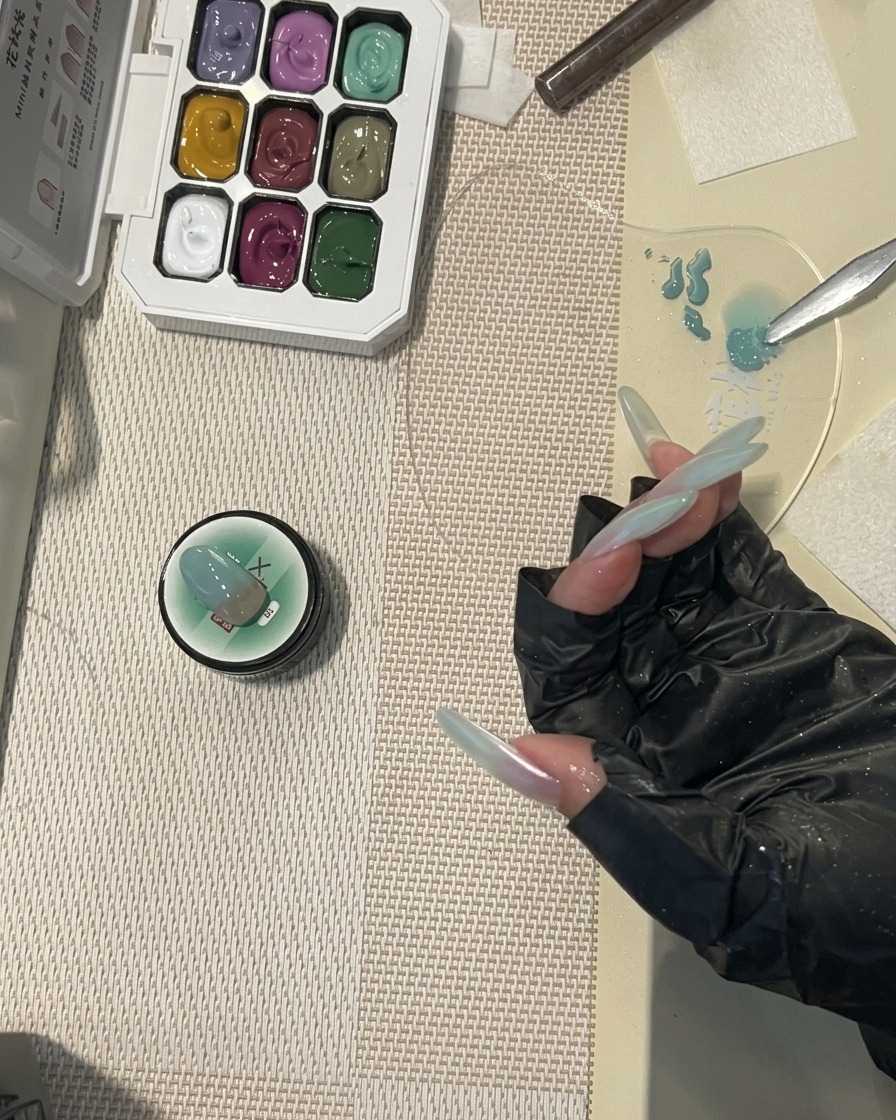 Ein Nagelpinsel trägt einen finalen, glänzenden Top Coat auf einen langen Nagel mit mintgrünem Verlaufsdesign auf.
