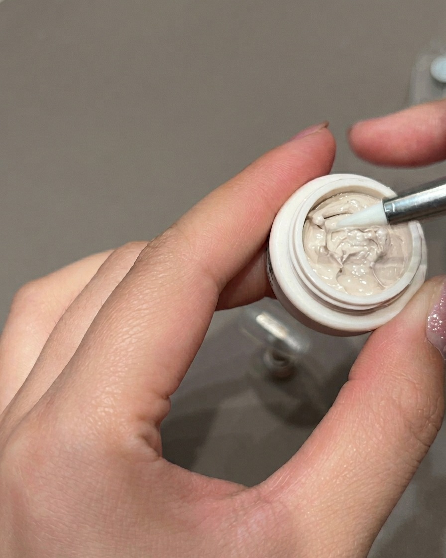 Eine Nahaufnahme eines Präzisions-Liner-Pinsels, der kleine braune Punkte auf einen mit Gel lackierten Nagel aufträgt.