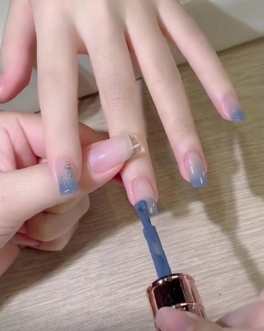 Ein Pinsel trägt rauchig-blaues Gel auf die Spitze eines vorbereiteten Fingernagels auf.