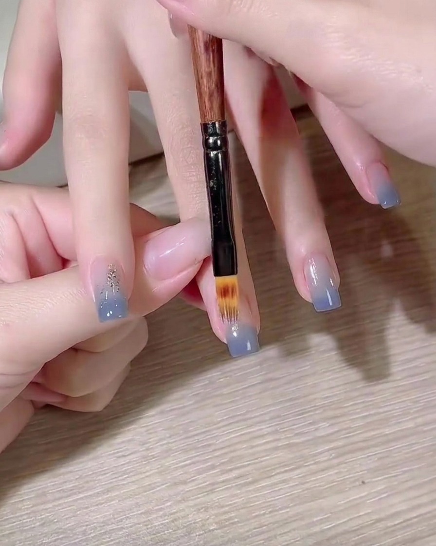 Ein flacher Gel-Pinsel verblendet einen blauen Farbverlauf auf dem Nagel.
