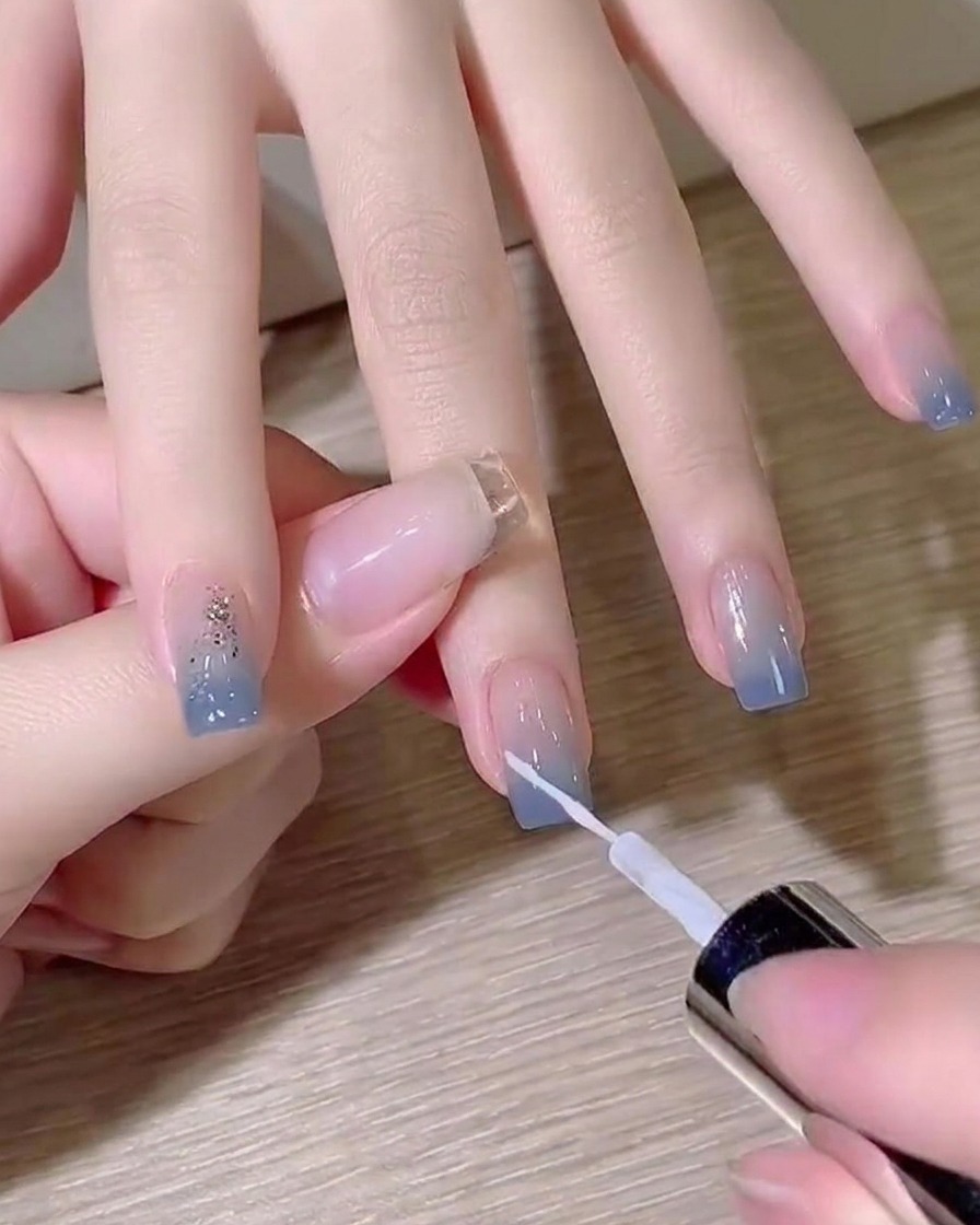 Ein feiner Liner-Pinsel zieht eine dünne weiße, diagonale Linie auf einem Ombré-Nagel.