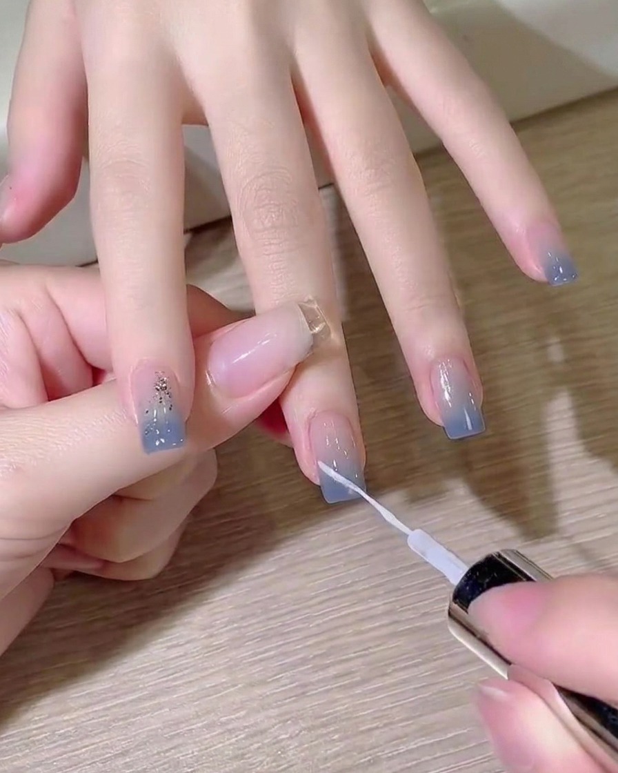 Ein feiner Liner-Pinsel malt eine scharfe weiße diagonale Linie über einen blauen Ombré-Nagel.
