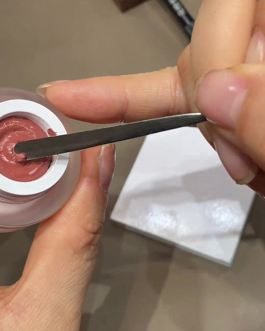 Ein Metallspatel gibt einen kleinen Klecks Farbgel auf eine weiße Palette.