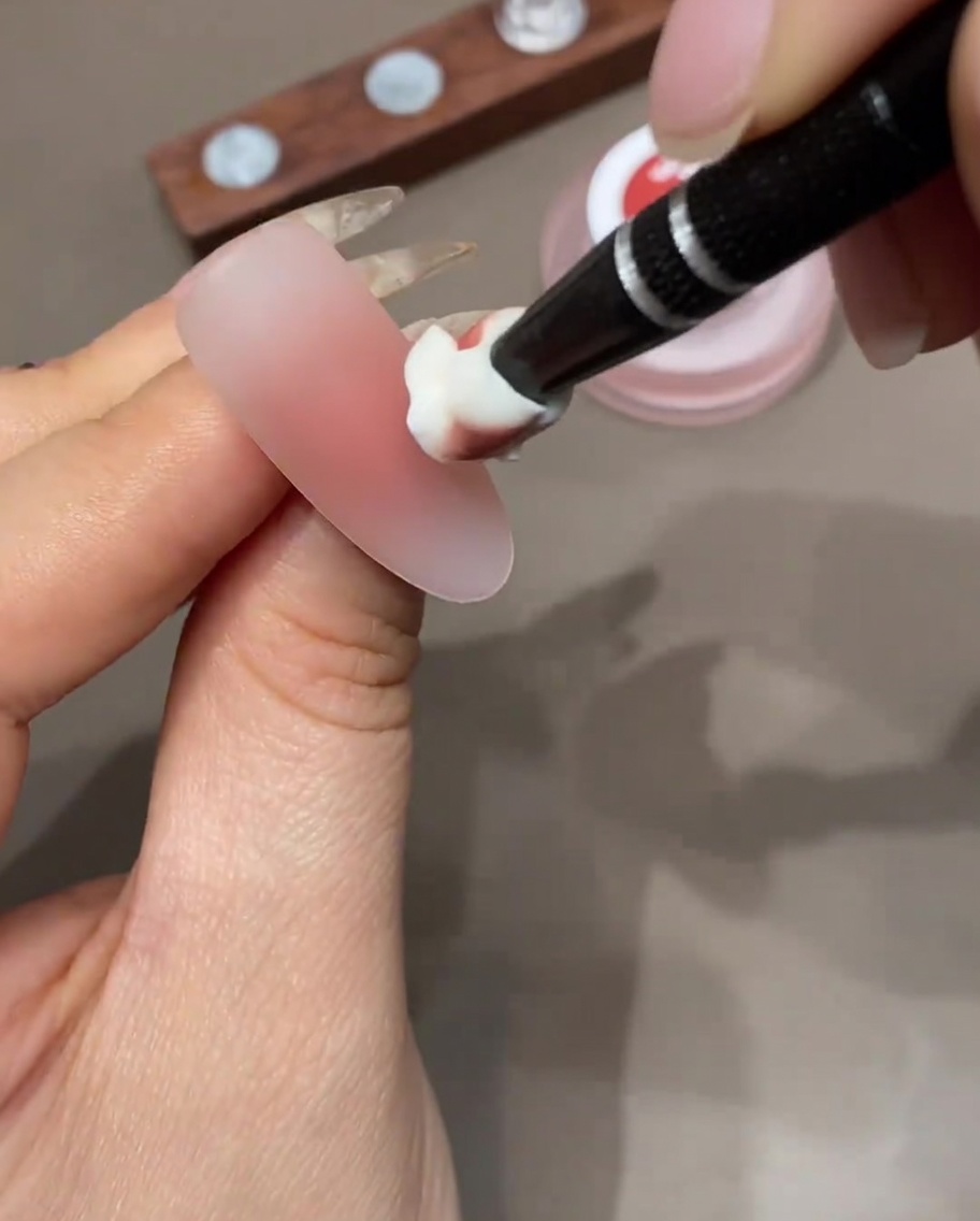 Ein Make-up-Schwamm trägt eine weitere Farbschicht auf die Nagelspitze auf.