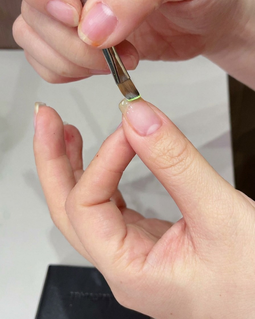 Nahaufnahme eines Detailpinsels, der hellgrünes Gel auf die freie Nagelspitze aufträgt.