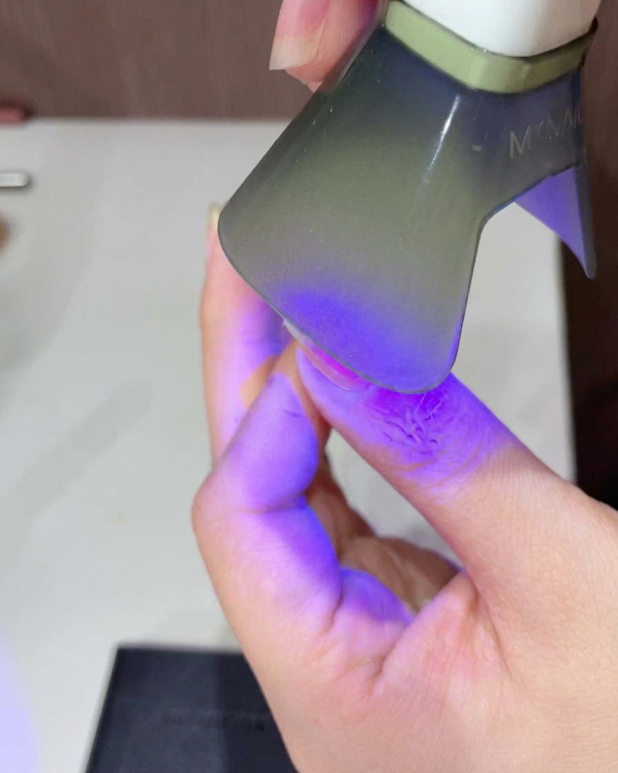 Nahaufnahme eines Fingers, der unter einer kleinen UV/LED-Lampe ausgehärtet wird.