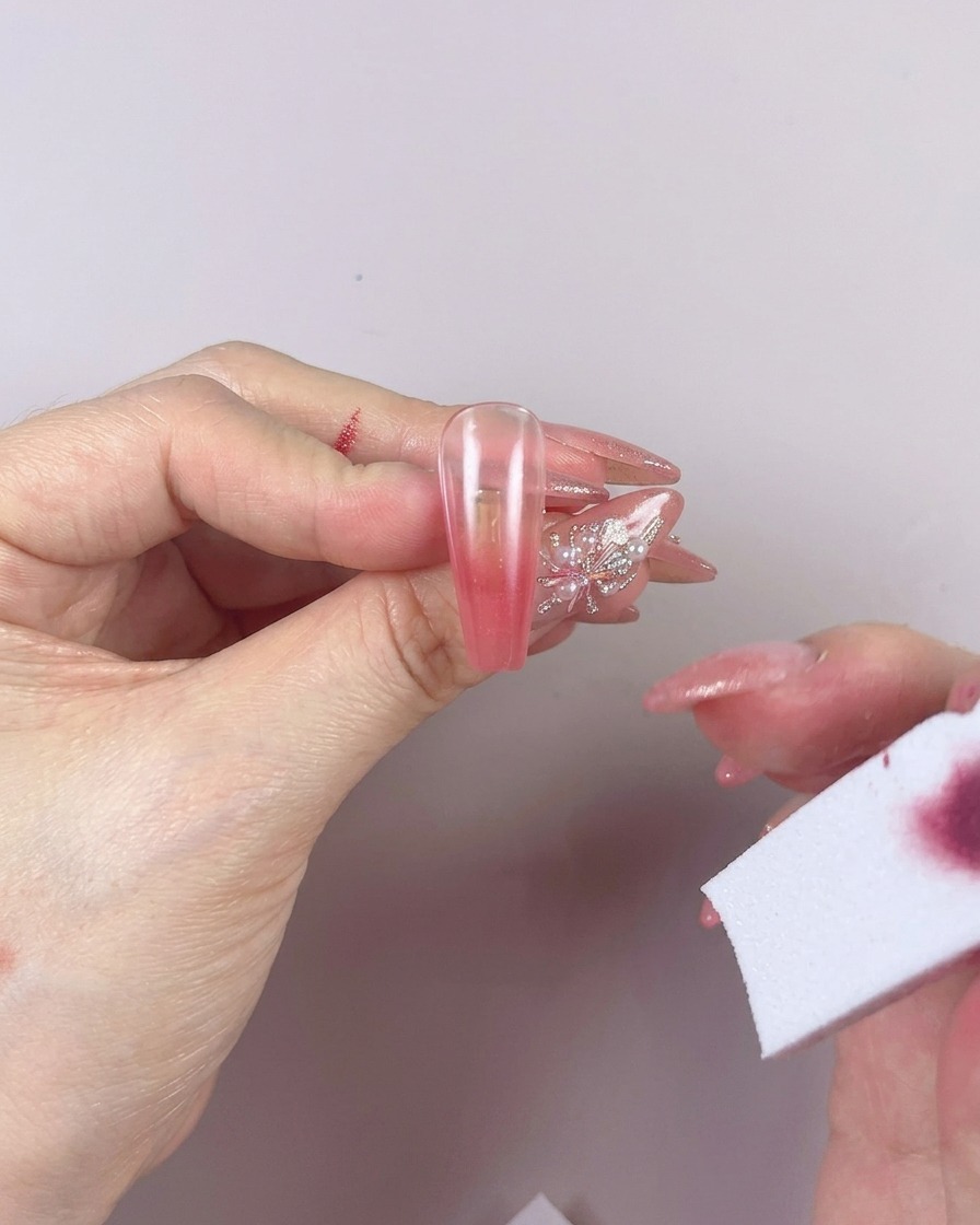 Ein Schwamm verblendet die Farbe auf dem Nagel mit horizontalen Bewegungen.