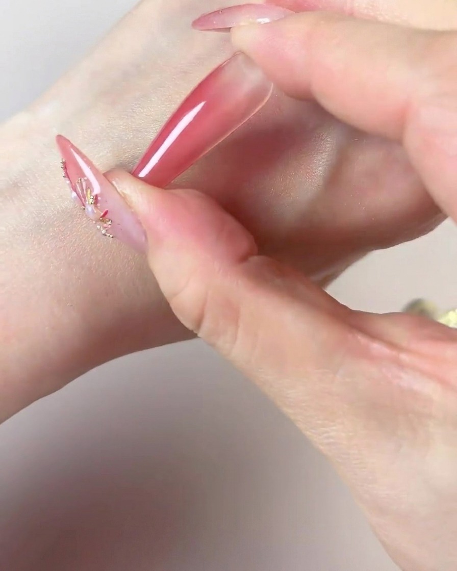 Eine Hand nutzt die dunkle Mitte eines Make-up-Schwamms, um Farbe an der Spitze eines langen Nagels zu intensivieren.