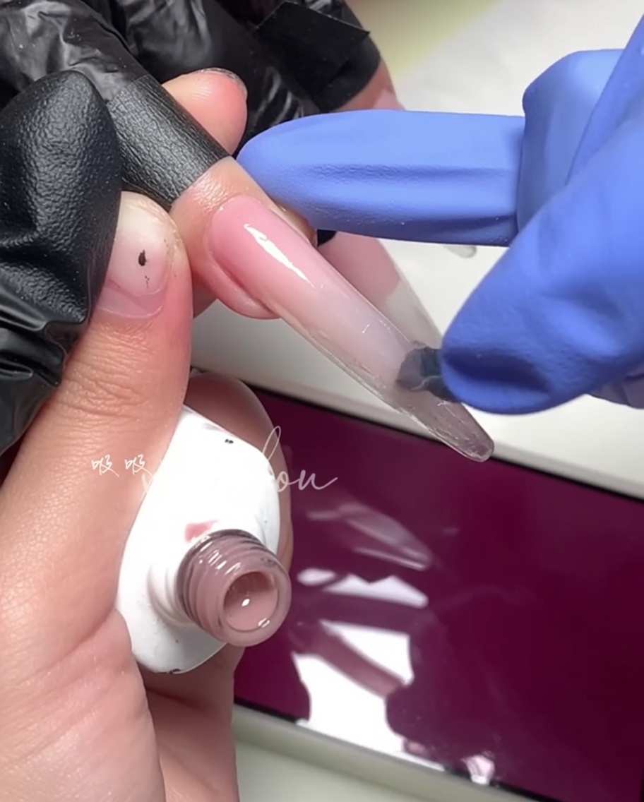 Nahaufnahme eines Pinsels, der ein helles Magenta-Gel auf die äußere Hälfte des Nagels aufträgt.