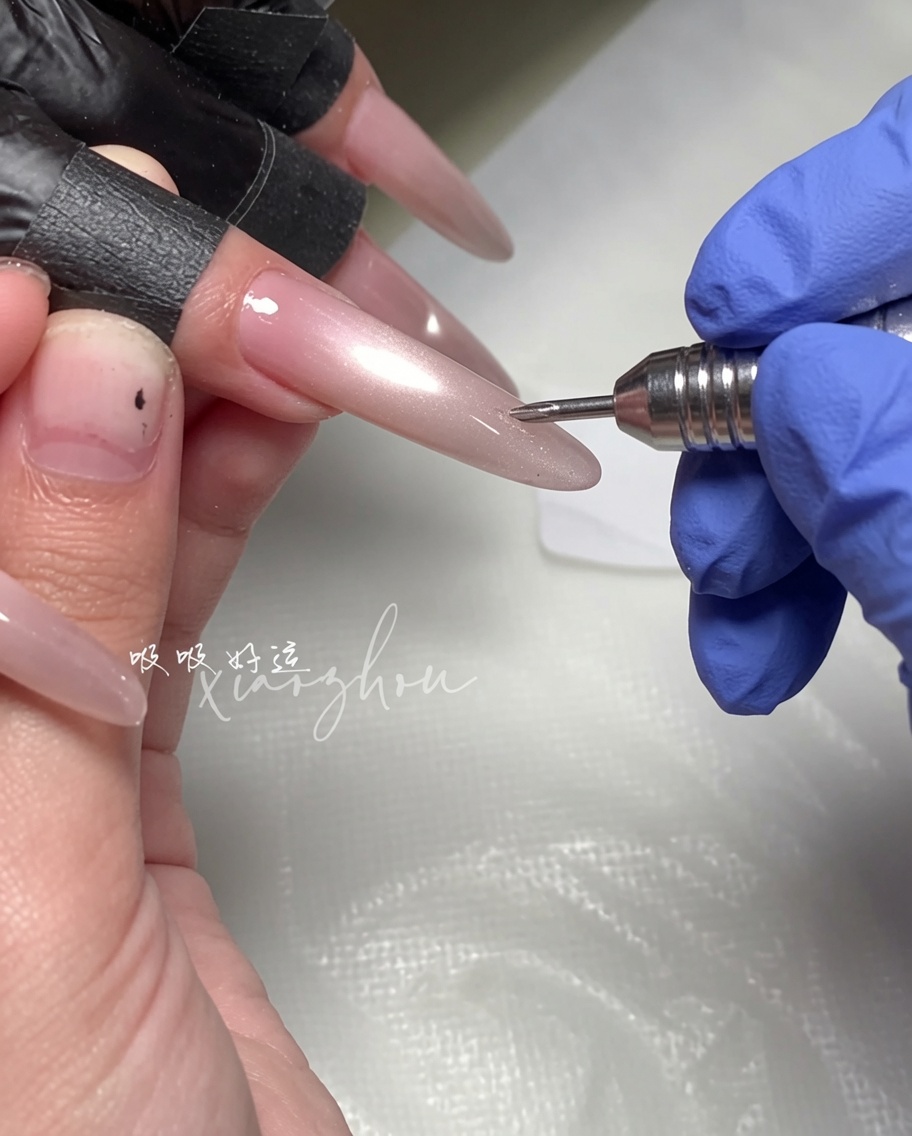 Eine Hand hält einen Magnetstab über einen langen, mandelförmigen Nagel, der mit feuchtem Magenta-Cat-Eye-Gellack beschichtet ist.
