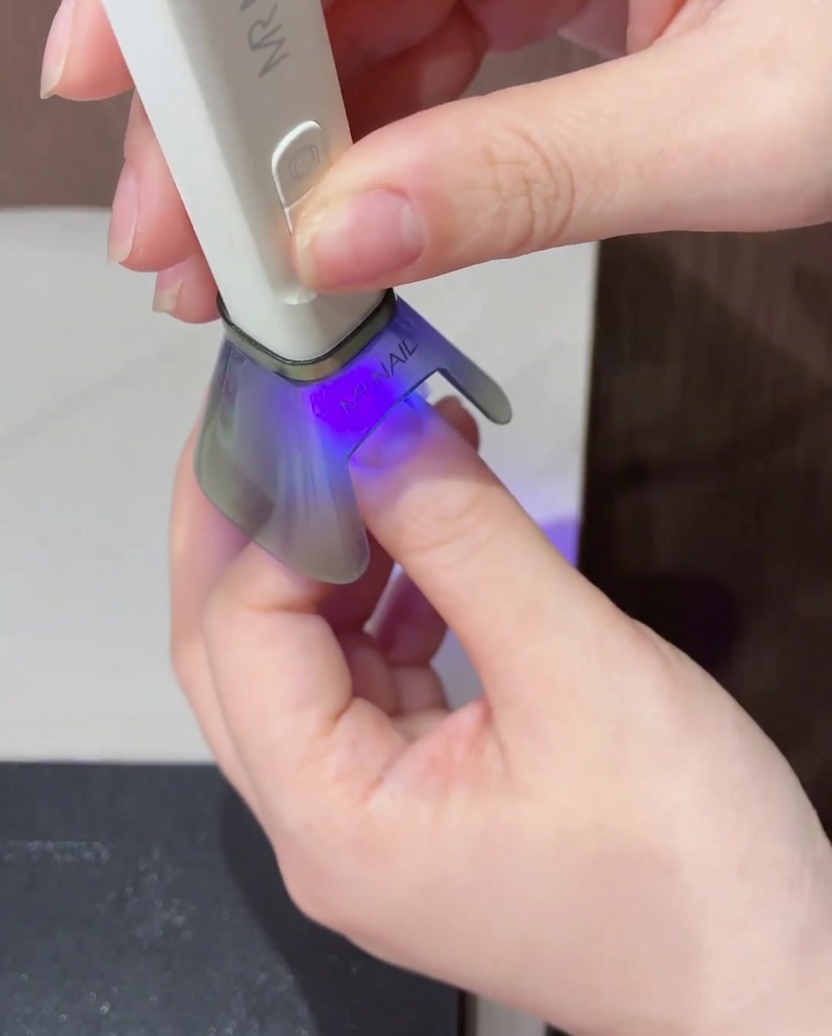 Nahaufnahme eines einzelnen Tropfens leuchtend gelben Gel-Lacks, der in die Mitte des Nagels mit der Magentaspitze aufgetragen wurde.