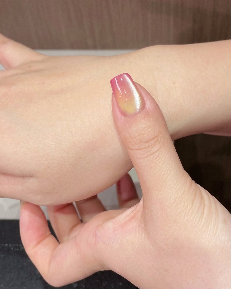 Ein Finger mit einem schimmernden Cat-Eye-Gradient-Nagel unter einer tragbaren UV-Lampe.