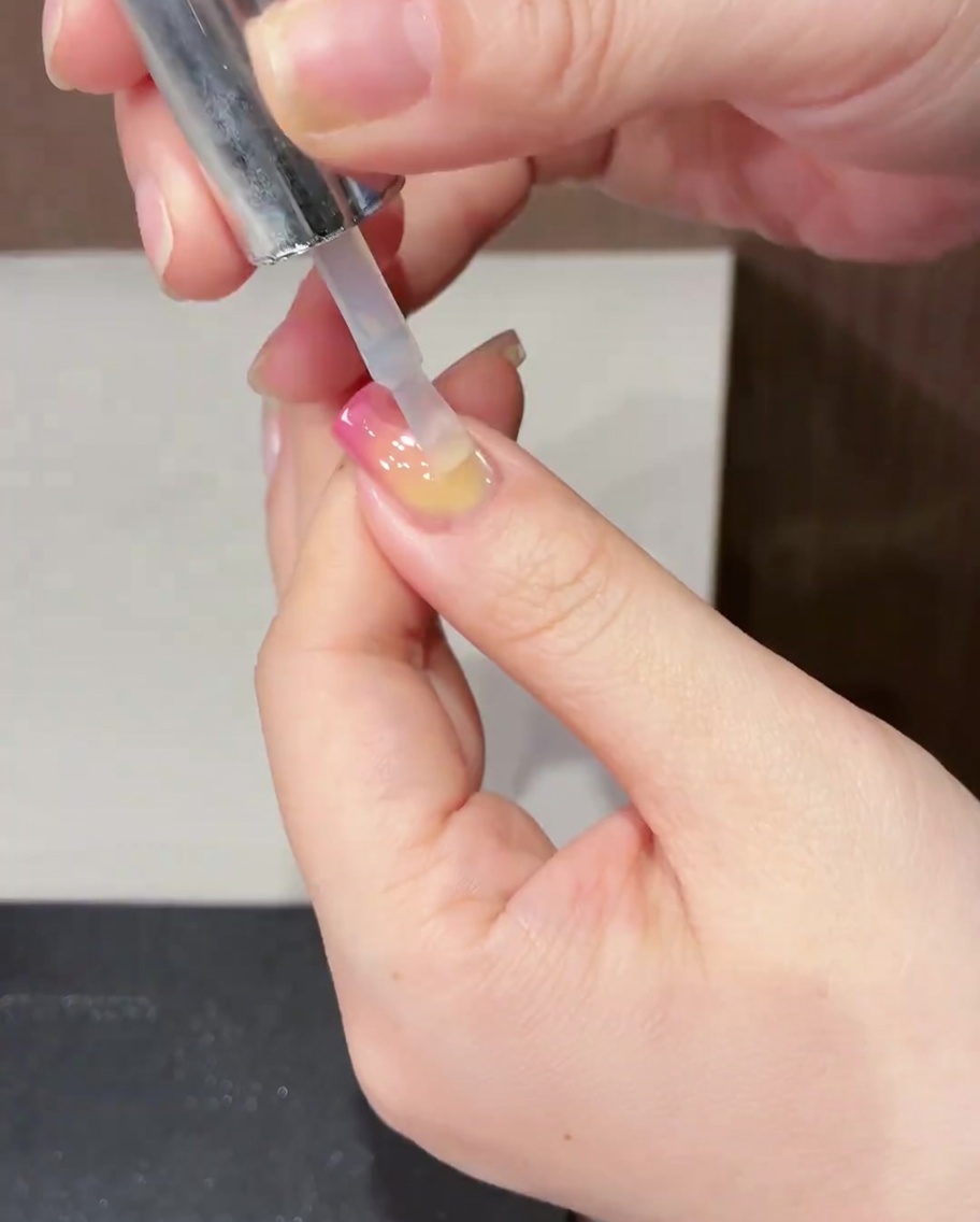 Ein Pinsel, der einen klaren, glänzenden Top Coat über ein fertiges Frühlings-Tulpen-Nageldesign aufträgt.