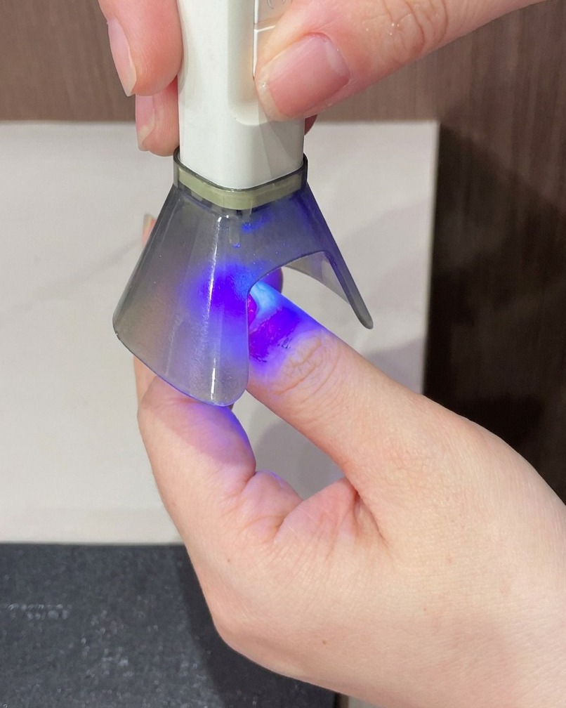 Ein Finger, der für den letzten Aushärtungsschritt der Maniküre unter eine tragbare UV-Lampe gehalten wird.