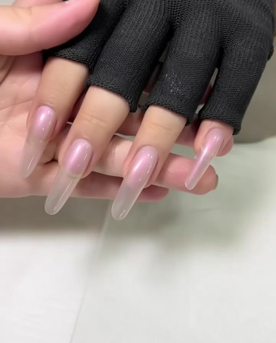 Nahaufnahme einer Hand mit langen, mandelförmigen Nägeln, bei der die Nagelhaut mit einem Metallschieber zurückgeschoben wird.