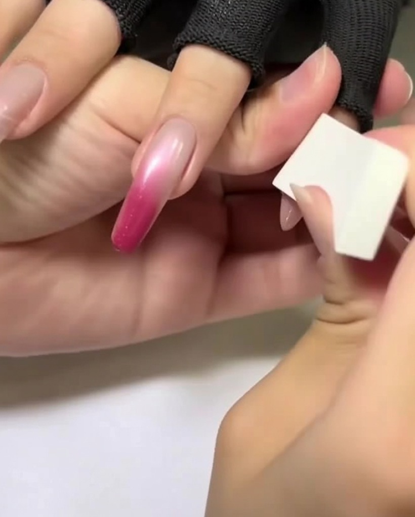 Eine Hand mit einem weißen Make-up-Schwämmchen trägt ein helles Rosa auf die obere Hälfte eines mandelförmigen Nagels auf.