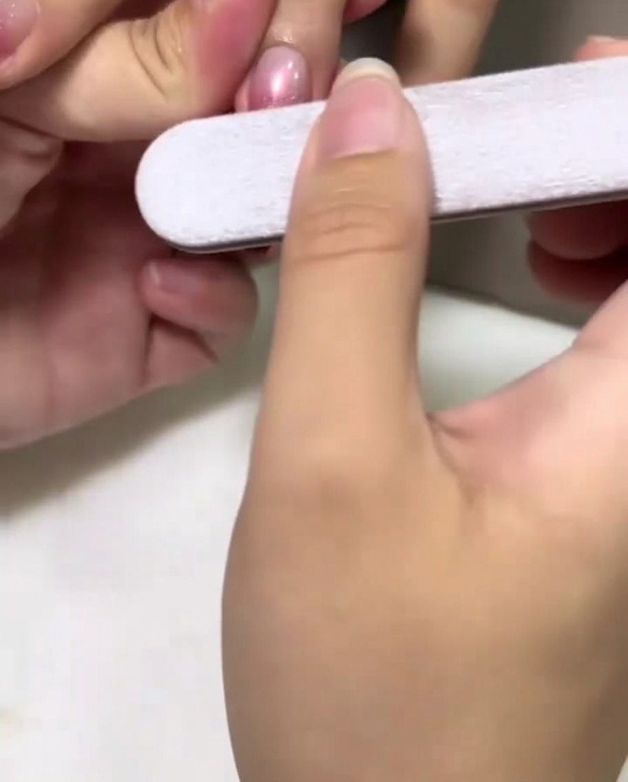 Eine Hand mit einer Nagelfeile mattiert sanft die Mitte eines rosa lackierten Nagels.