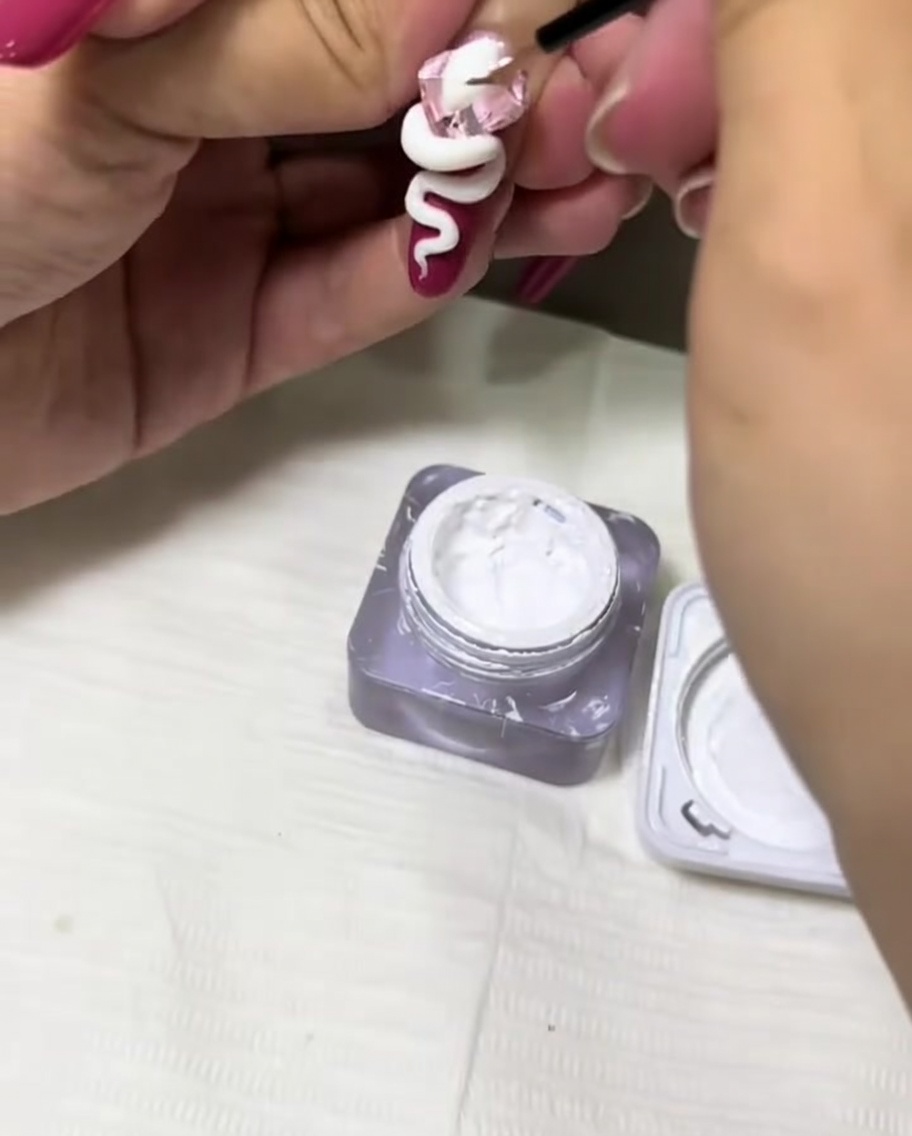 Ein dünner Detailpinsel trägt weißes Gel auf, um einem 3D-Schlangendesign auf einem Nagel Struktur zu verleihen.