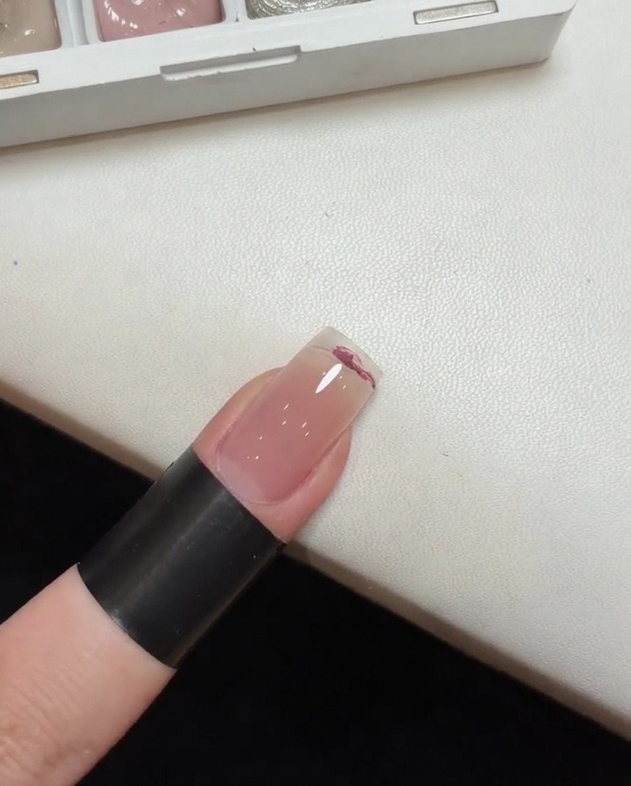Ein Schwamm-Werkzeug tupft und verblendet rosa Gellack auf einem Nagel, um einen Ombré-Effekt zu erzeugen.