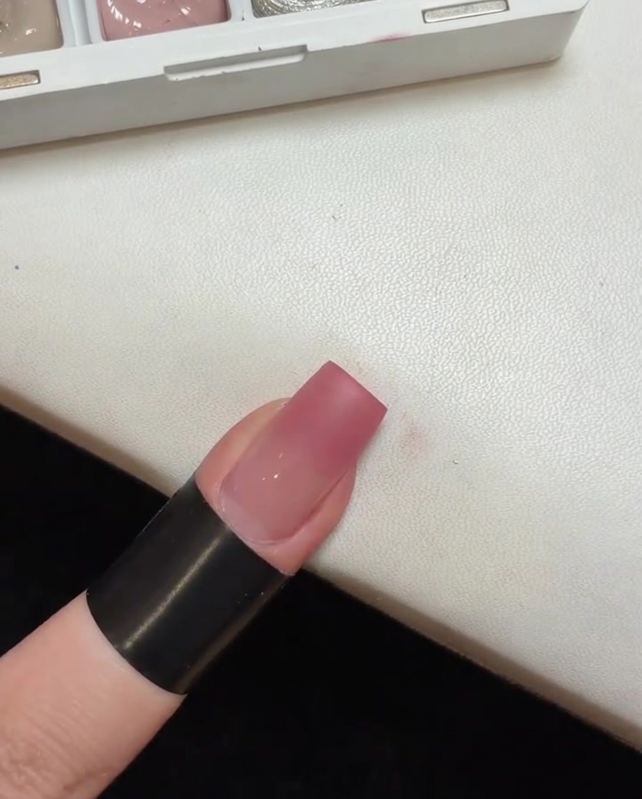 Ein Nagel mit einer rosa Ombré-Basis härtet in einer kleinen, tragbaren UV-Lampe aus.