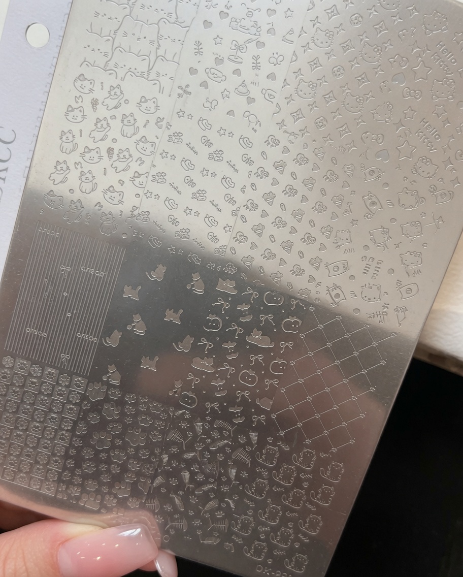Eine dünne Schicht altrosafarbener Gellack wird über ein Kitty-Muster auf einer Stamping-Schablone aus Metall aufgetragen.