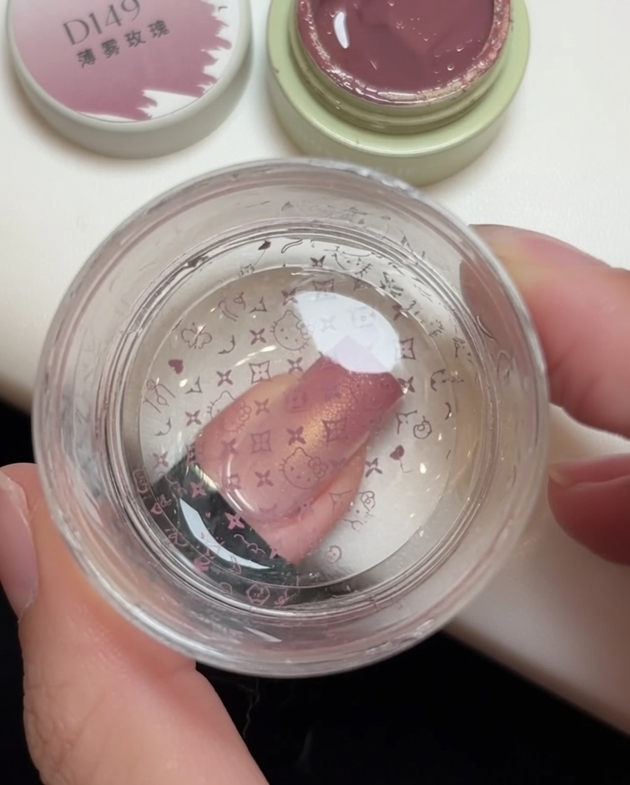 Ein Jelly-Stamper drückt ein rosa Muster auf einen Nagel, wobei das Hello Kitty Design auf dem Stempelkopf sichtbar ist.