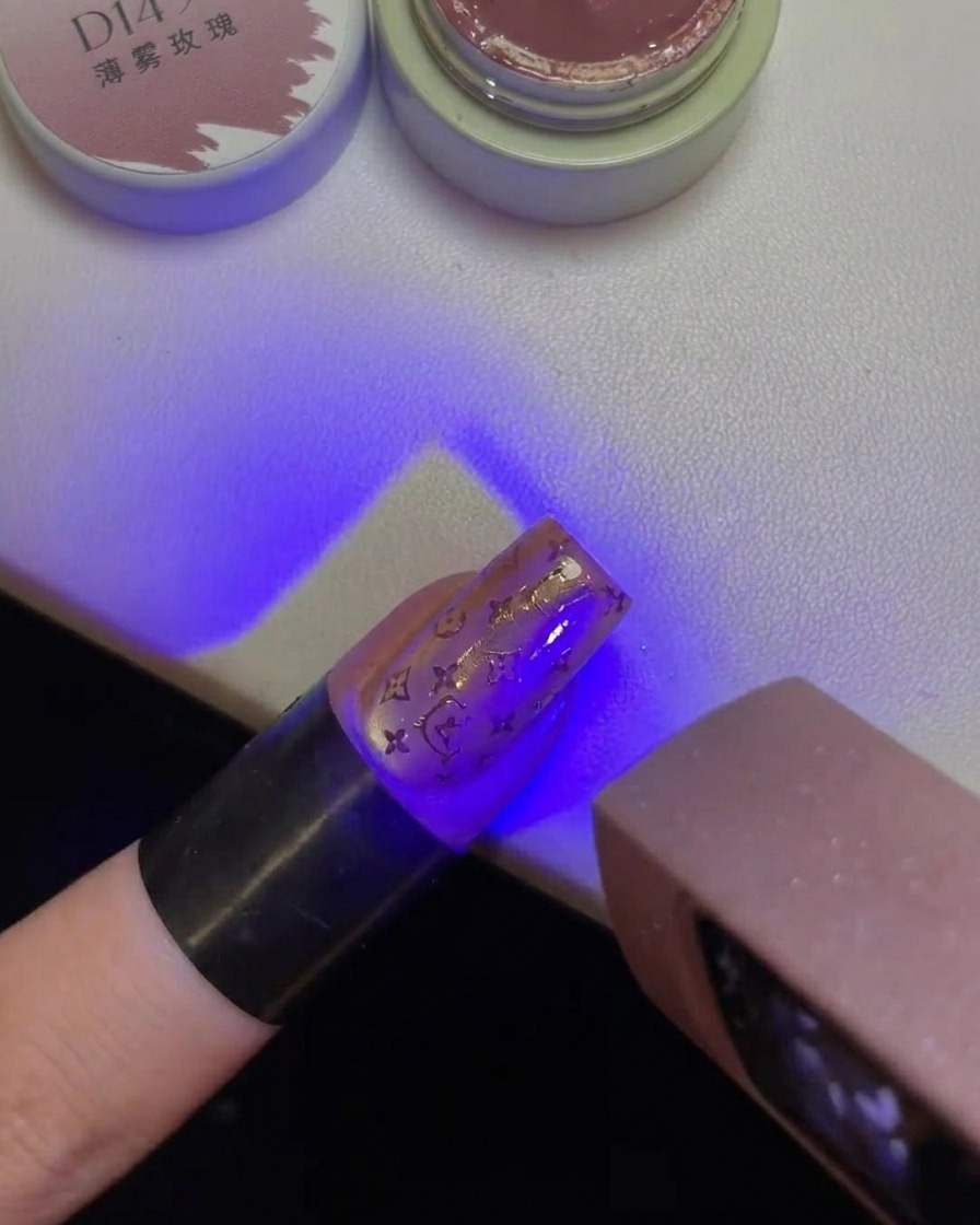 Ein Finger mit einem gestempelten Hello Kitty Design auf dem Nagel wird unter das lila Licht einer UV-Lampe gehalten.