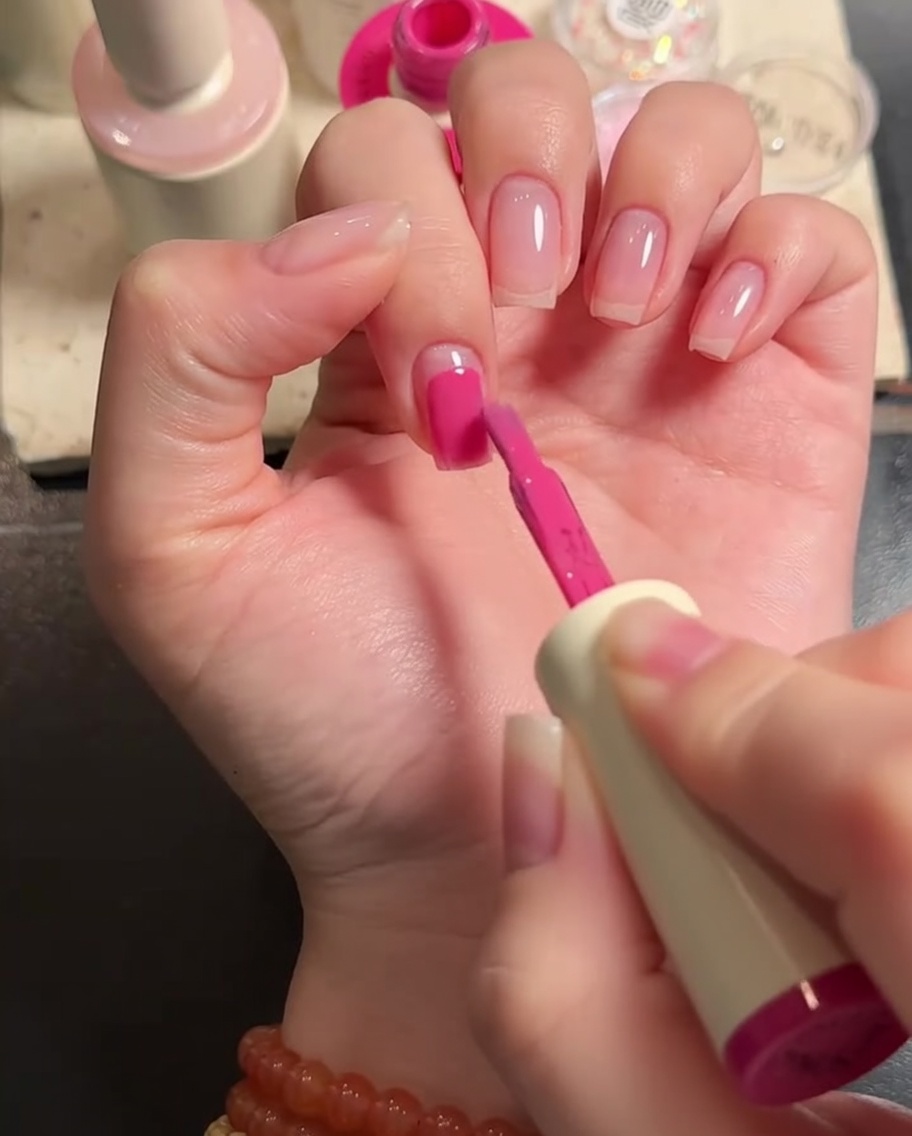 Ein flacher Nagelpinsel trägt rosa Gelpolitur auf die Nagelplatte auf.